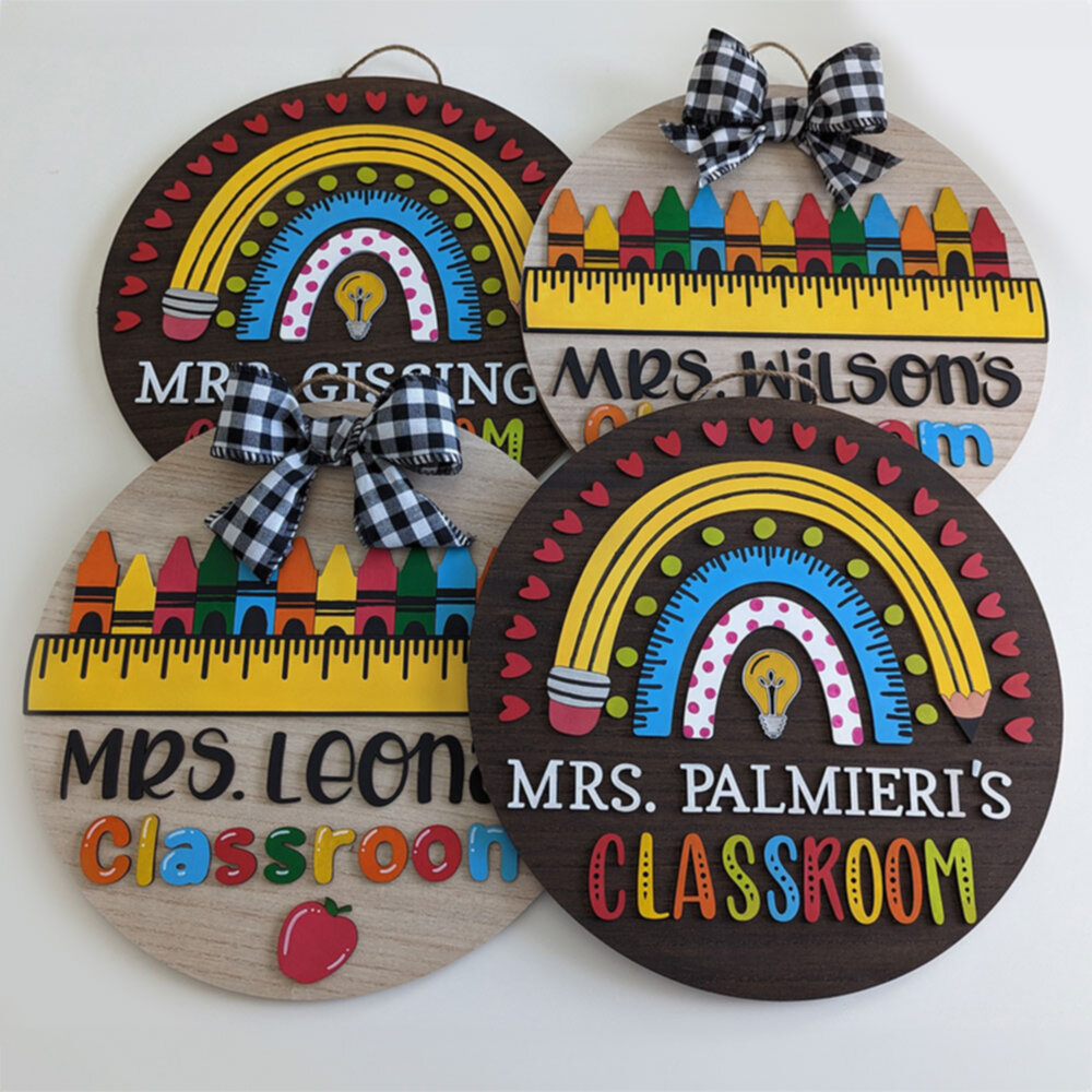 Four custom teacher classroom signs laid out, each with bright designs including rainbows, rulers, crayons, hearts, and teacher names.