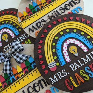 Artistic top view of multiple colorful classroom signs overlapping, showcasing unique teacher names, rainbows, and crayon motifs.