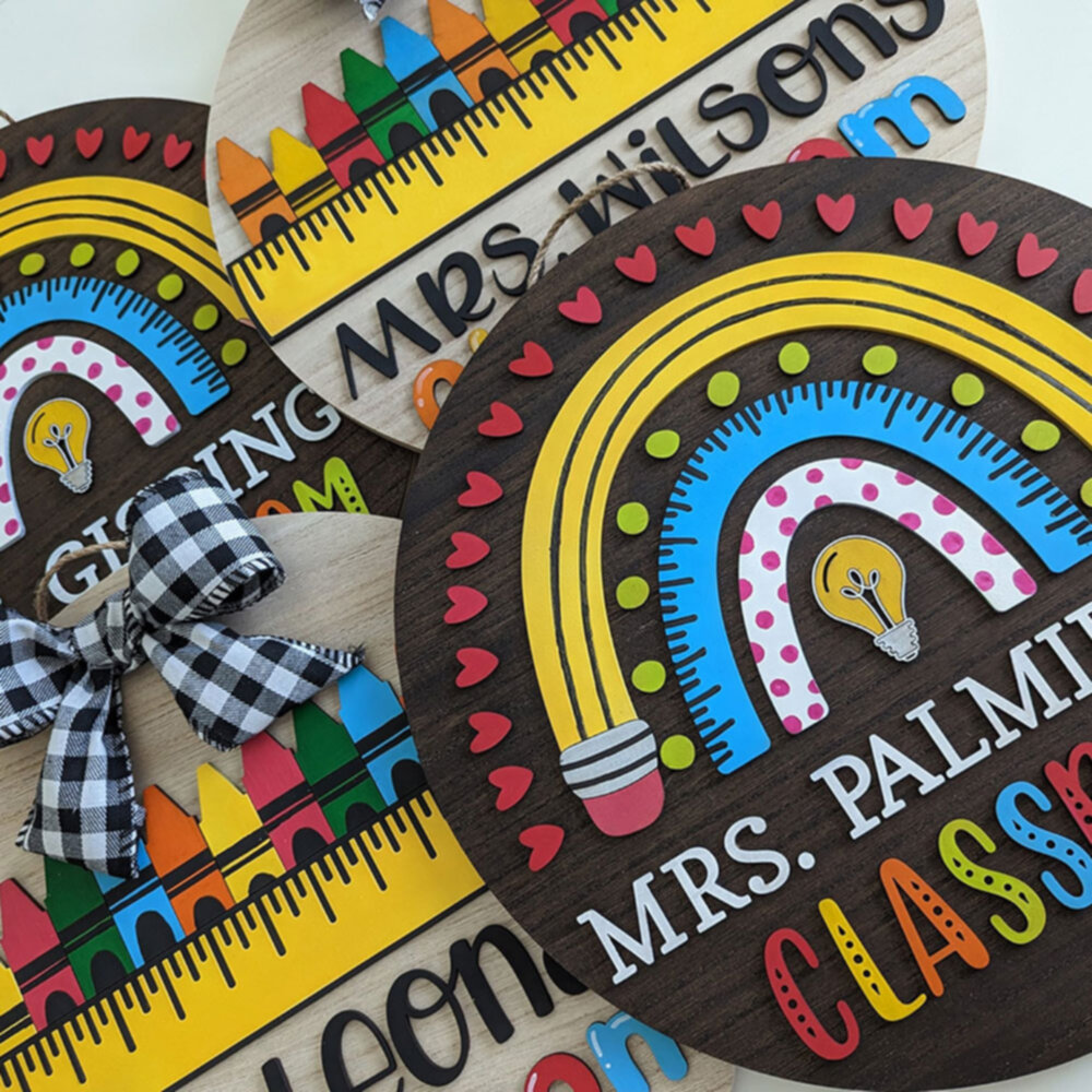 Artistic top view of multiple colorful classroom signs overlapping, showcasing unique teacher names, rainbows, and crayon motifs.