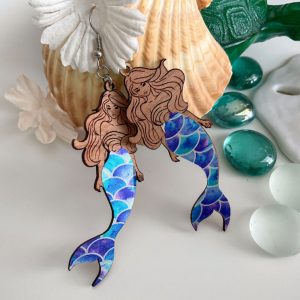 Mermaid earrings styled with seashells and aqua glass pebbles, featuring wooden upper sections and blue-scale tails.