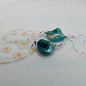 Pair of handmade dangle earrings featuring translucent teardrop-shaped charms with white daisy patterns and irregular blue-green pearl-like beads, displayed on a white textured background.