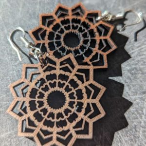 Close-up of intricate mandala-style wooden earrings casting a shadow on a gray textured surface.
