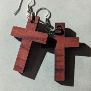 Close-up of wooden cross earrings with silver hooks casting shadows on a light textured surface.