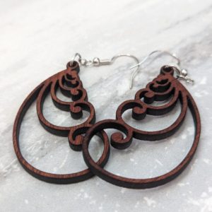 Detailed view of ornate wooden swirl teardrop earrings laid on a marble surface.