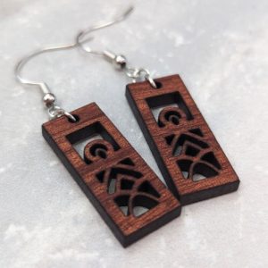 Geometric wooden earrings with silver hooks displayed on a light gray stone background.