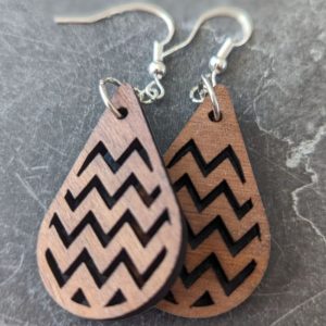 Detailed view of two medium-toned wood earrings featuring laser-cut chevron patterns on a stone background