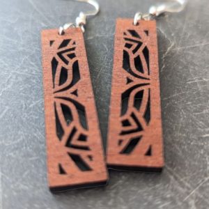 Close-up of rectangular laser-cut wood earrings with geometric motif on slate surface