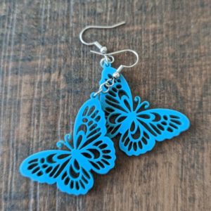 Two teal butterfly cutout earrings with fishhook wires on a wooden tabletop