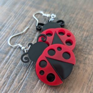 Ladybug-shaped earrings with curled antennae resting on a wooden surface.