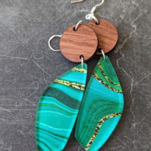 Pair of handmade earrings featuring green marbled acrylic teardrops and circular walnut wood tops, displayed on a dark slate surface.