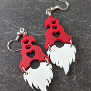 Fun gnome earrings featuring red hats with heart cutouts and dangling white beards on a dark stone background.