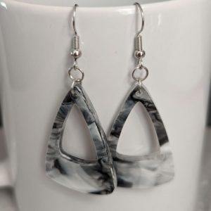 Black and white marbled acrylic triangle earrings with open centers, hanging on the rim of a white ceramic mug for display.