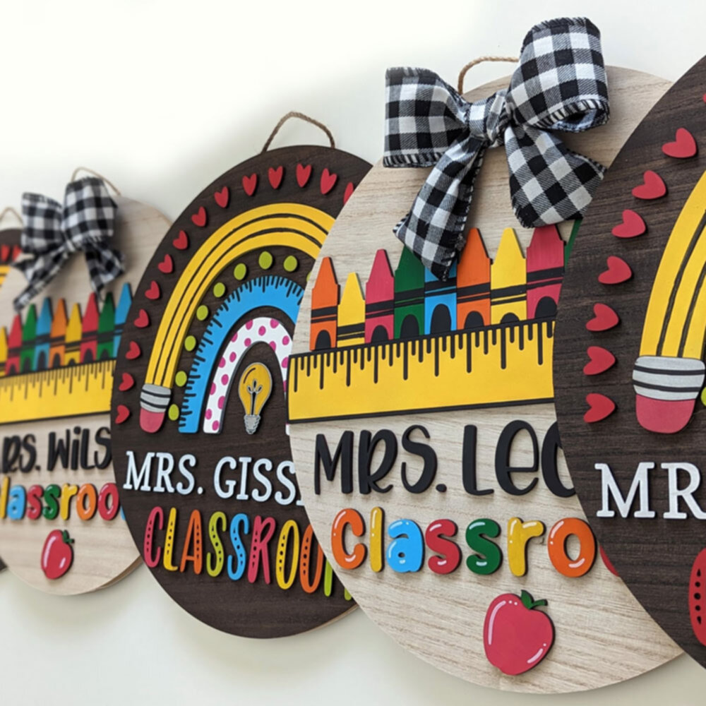Row of colorful, round wooden classroom signs featuring teacher names, rainbows, pencils, rulers, crayons, and gingham ribbon bows.
