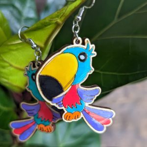 Close-up of parrot-shaped earrings hanging on a green plant, highlighting their bright tropical hues and cheerful style.