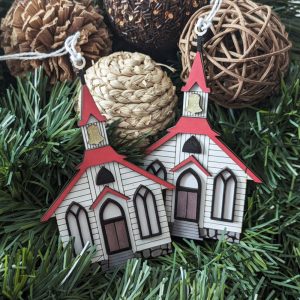 Two wooden church ornaments with red roofs and gold bell towers displayed on pine greenery and surrounded by decorative natural elements like pinecones and woven balls.