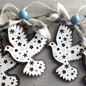 Set of layered wooden dove ornaments with star and circle cutouts, each tied with rustic ribbon and a blue wooden bead, displayed on a gray background.