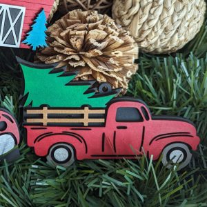 Rustic red truck Christmas ornament with a green tree in the back, styled with pinecones and natural decor.
