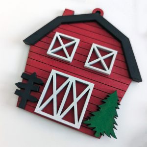 Close-up of a red barn-shaped Christmas ornament with white trim, green tree detail, and directional sign
