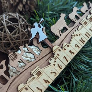 Wooden nativity countdown calendar featuring angel, camels, and animals with engraved buildings and numbers over pine background.