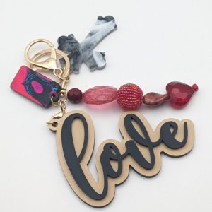 Keychain with gold and black "love" text, gray marbled cross, and a row of vivid red and pink beads including a beaded ball and heart charm.