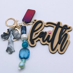 Keychain with "faith" script in gold and black, gray marbled cross charm, and a strand of pearls and faceted blue and teal beads, with a pink rhinestone accent on the word.