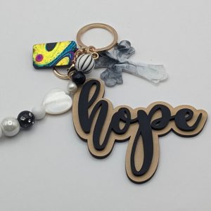 "Hope" keychain in black and gold, paired with a marbled gray cross charm and elegant black, white, and pearl-toned beads including a mother-of-pearl heart.