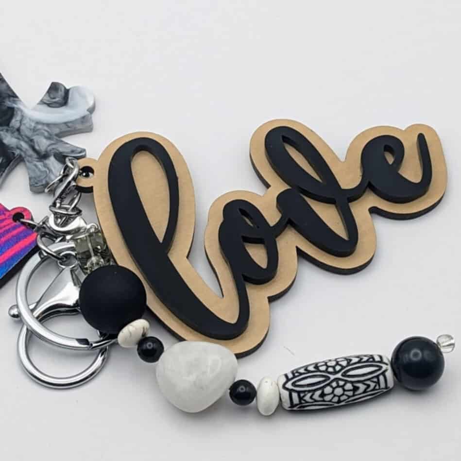 Keychain with "love" word charm, gray and white marbled cross, and monochrome beads in black and white with tribal-style design.